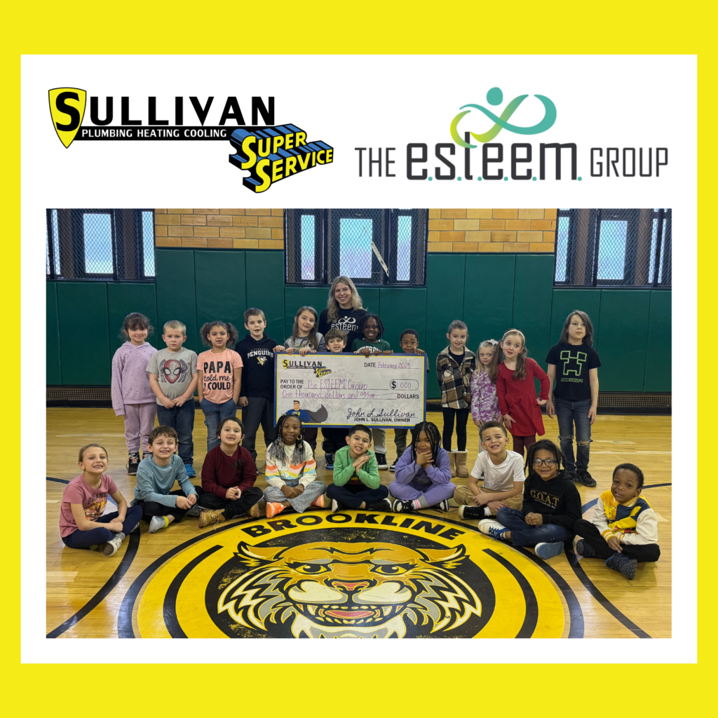 A group of children and adults pose in a gym, holding a large check, with business logos and a school tiger mascot on the floor.