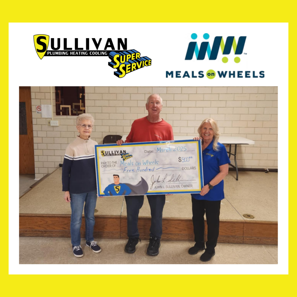 Three people stand indoors holding a large check from Sullivan Plumbing Heating Cooling to Meals on Wheels for $500. Sullivan and Meals on Wheels logos appear above them.