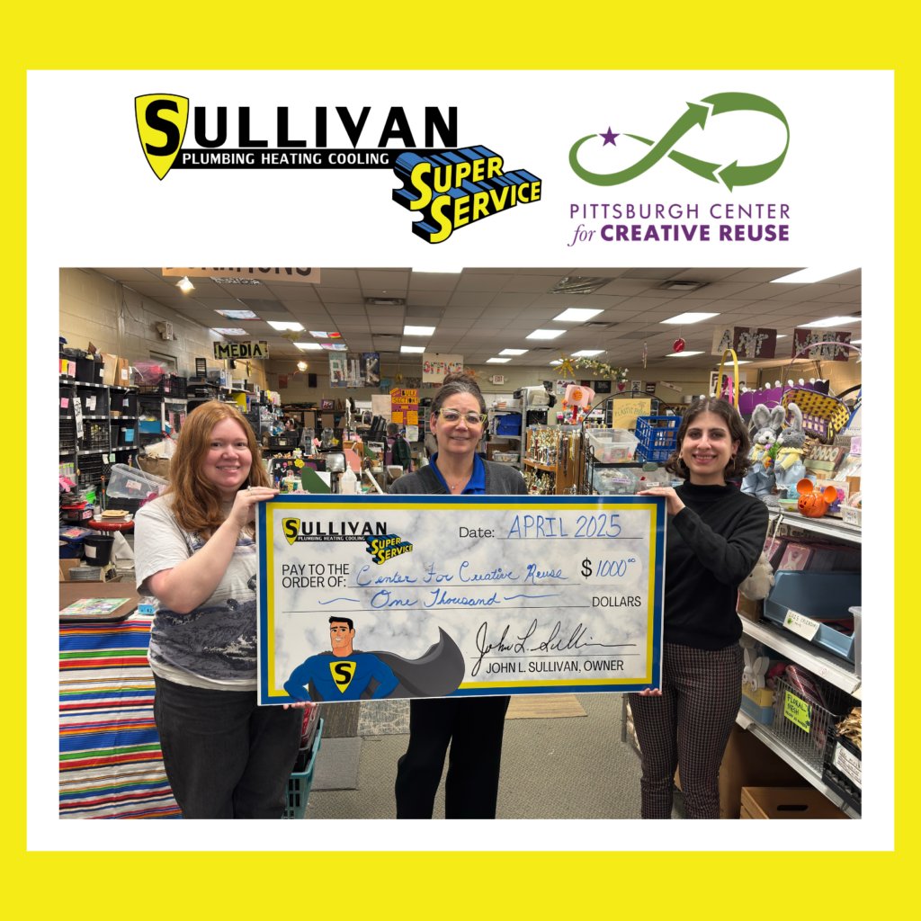 Three women stand in a store holding a large check for $1,000 from Sullivan Plumbing Heating Cooling to the Pittsburgh Center for Creative Reuse, dated April 2025.